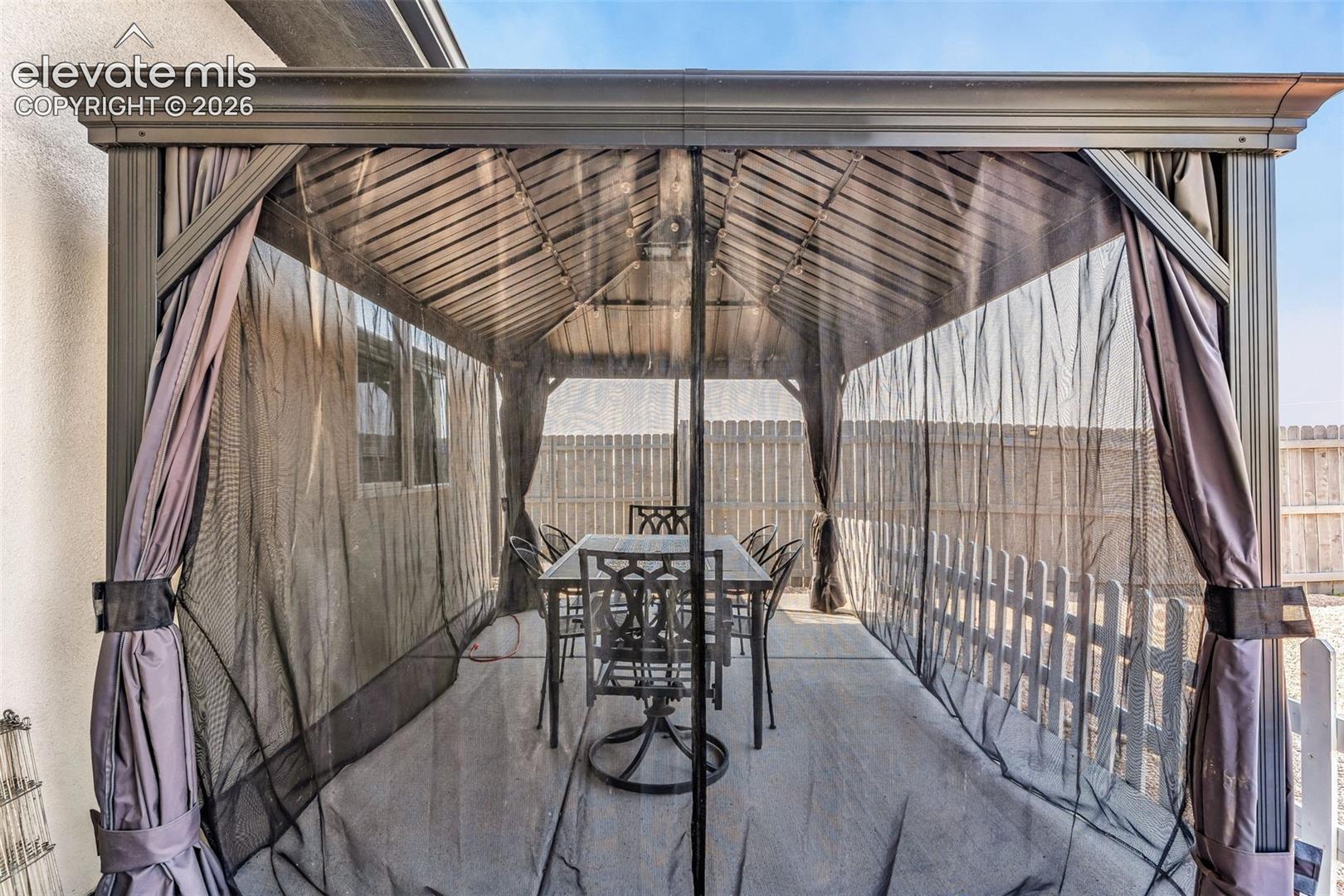 Outdoor gazebo featuring a slatted roof, fabric privacy screens, and a concrete patio foundation
