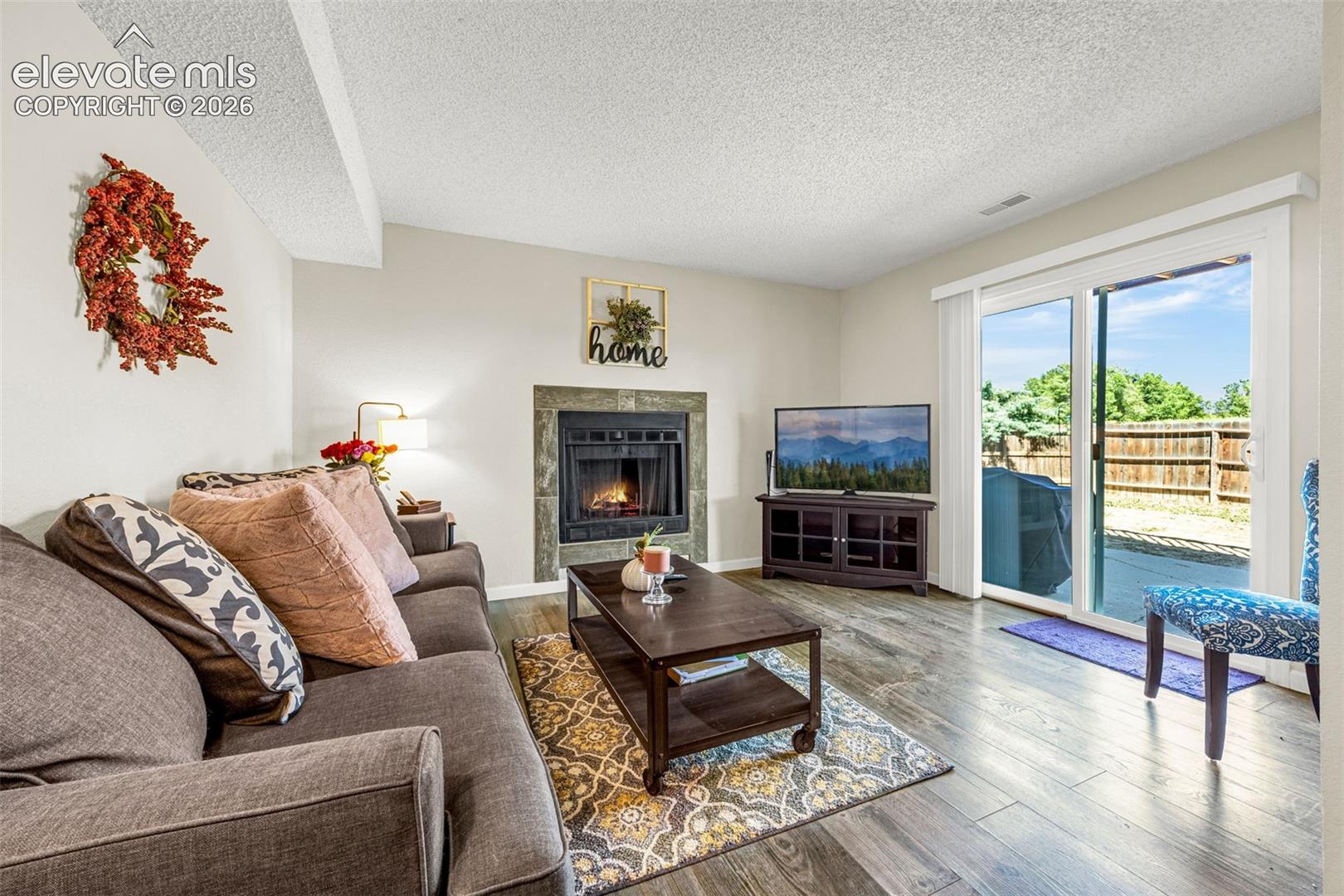 Living area featuring wood-finish flooring, a fireplace with a stone-tile surround, and a sliding glass door providing access to the exterior