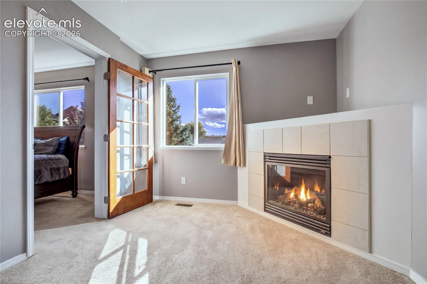 French doors open from the primary suite to the cozy private sitting room/office featuring the home's second gas fireplace + a large window.