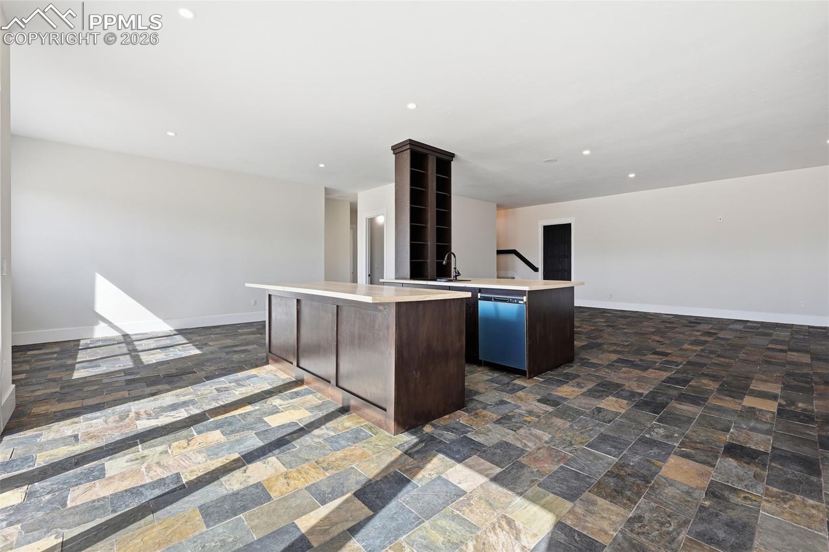  Lower Level Famiy Room featuring light countertops, dark wood finish cabinetry, a center island with sink, stainless steel dishwasher, and dark stone finish floors
