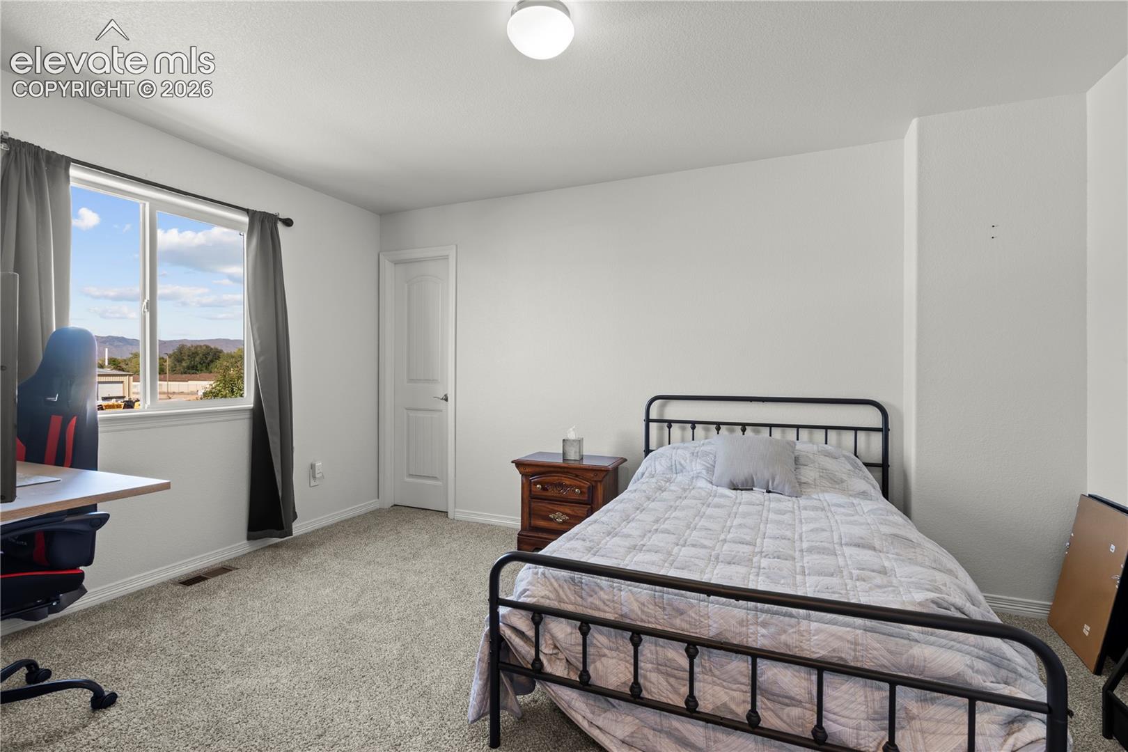Neutral-toned interior room featuring wall-to-wall carpeting, a multi-pane window with exterior mountainous scenery, and a single-panel interior door with brushed metal hardware
