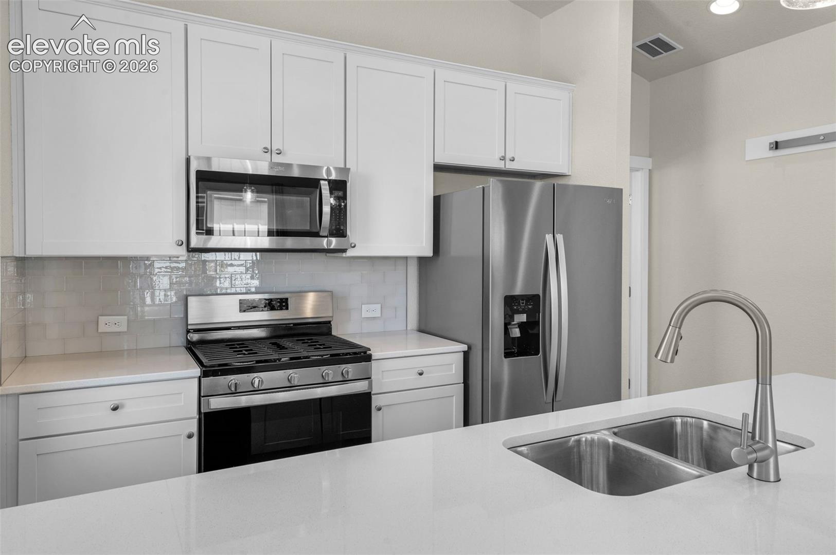 Kitchen featuring white shaker-style cabinetry, stainless steel appliances, subway tile backsplash, quartz countertops, and a dual-basin undermount sink with a high-arc faucet