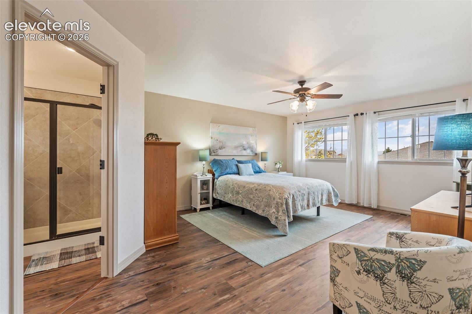 Spacious room featuring wood-finish flooring, two window openings, and a ceiling fan with integrated lighting
