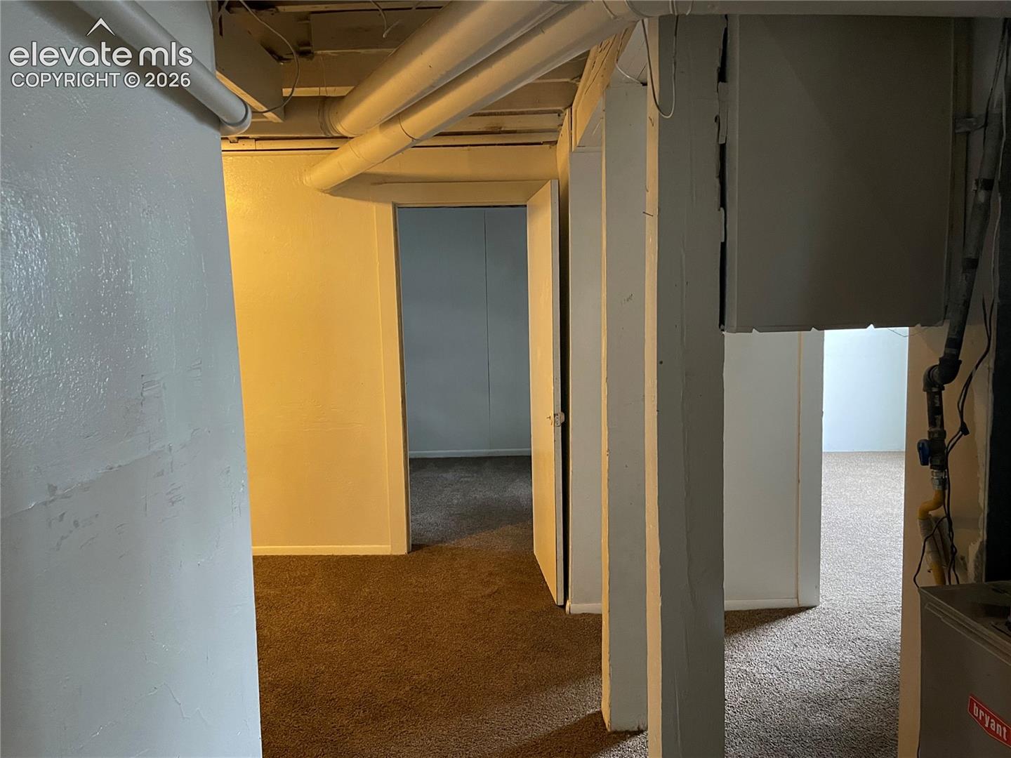 Finished basement space featuring brown carpeting, white painted walls, exposed ceiling pipes, and multiple doorways
