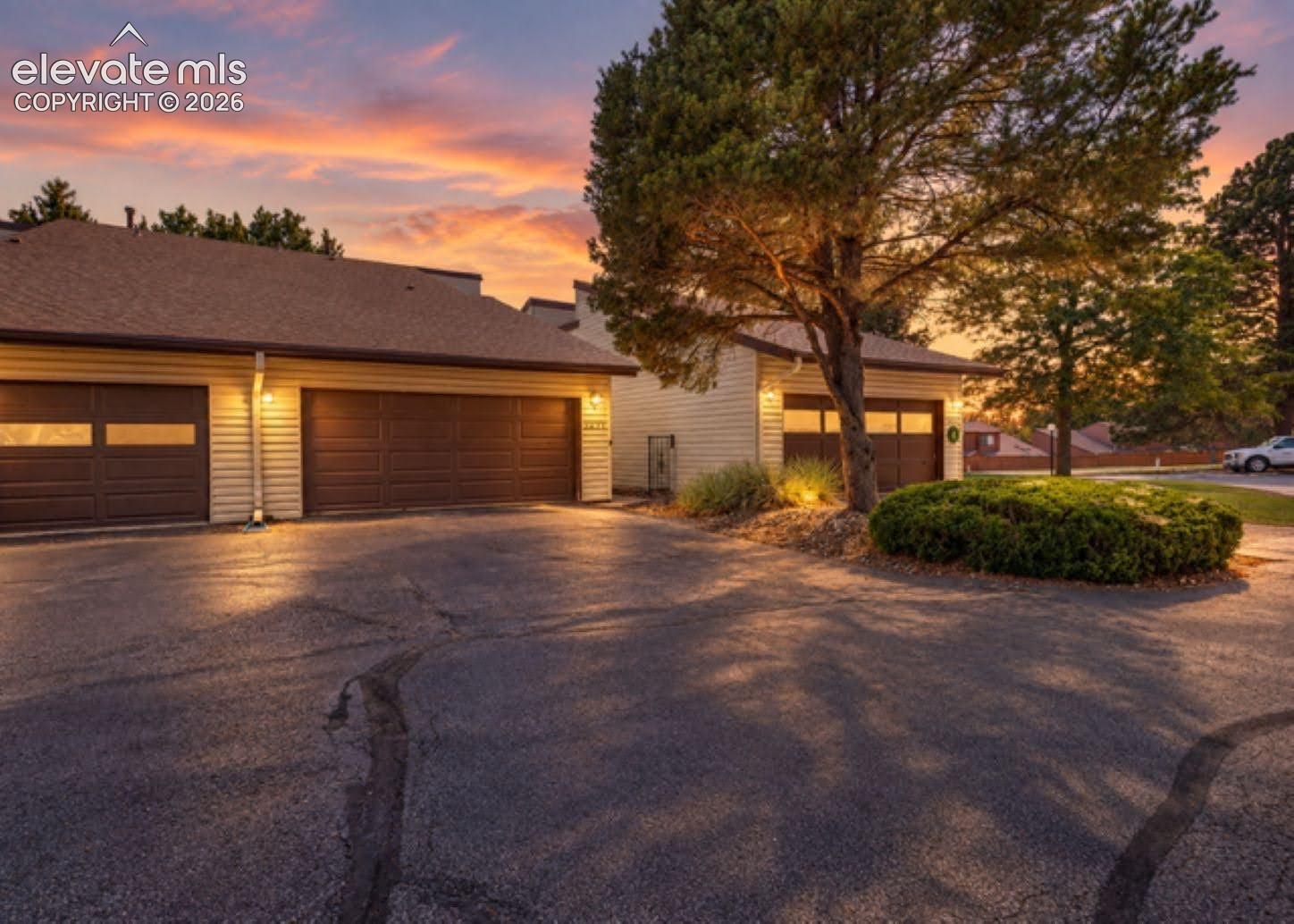 Multi-car garage exterior with horizontal siding, paneled garage doors, asphalt driveway, and mature landscaping