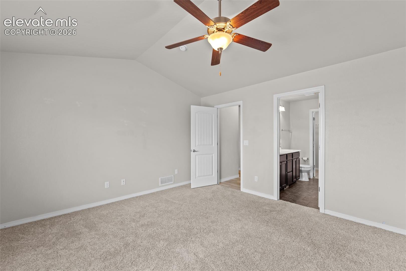 Spacious bedroom featuring neutral wall finishes, plush carpeting, ceiling fan with integrated lighting, and dual closet access