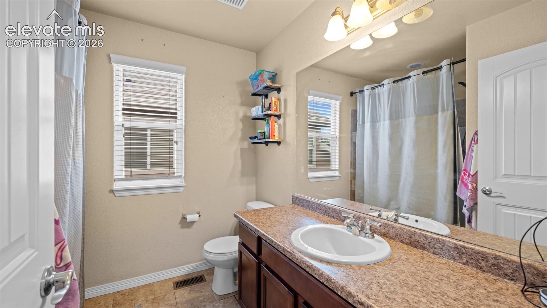 Bathroom featuring a single vanity with a patterned countertop, a built-in sink, and a large wall-mounted mirror