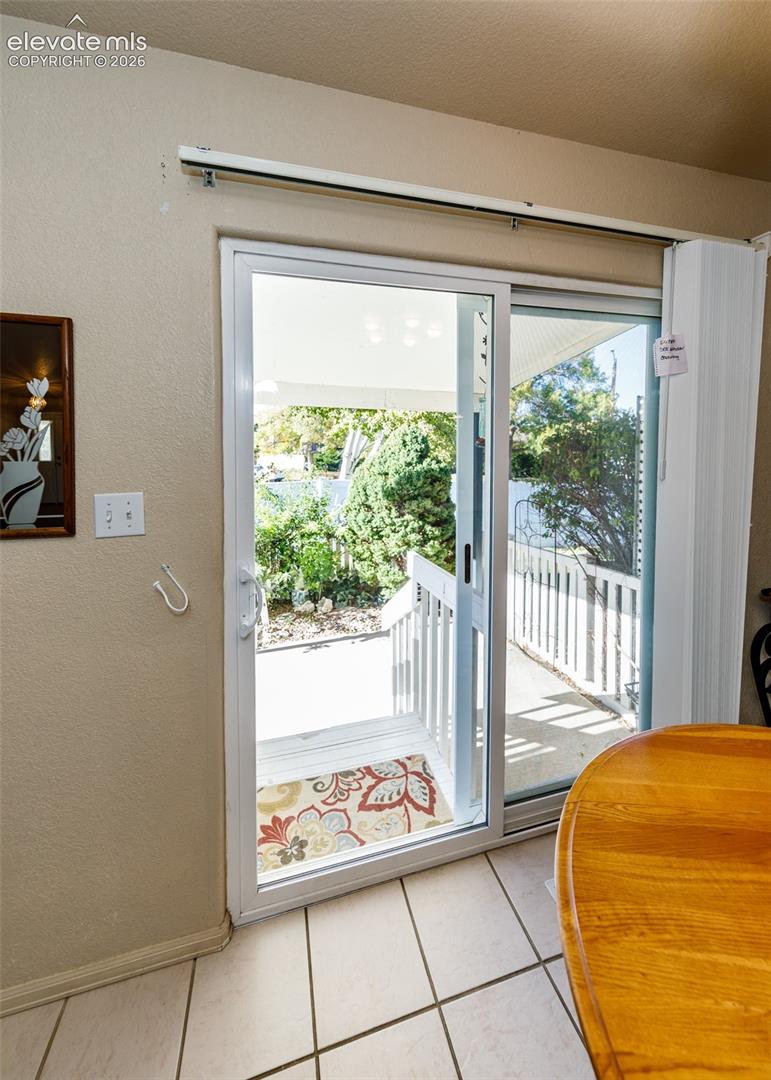 Sliding glass door with white framing, ceramic tile flooring, and exterior wood deck with white railing