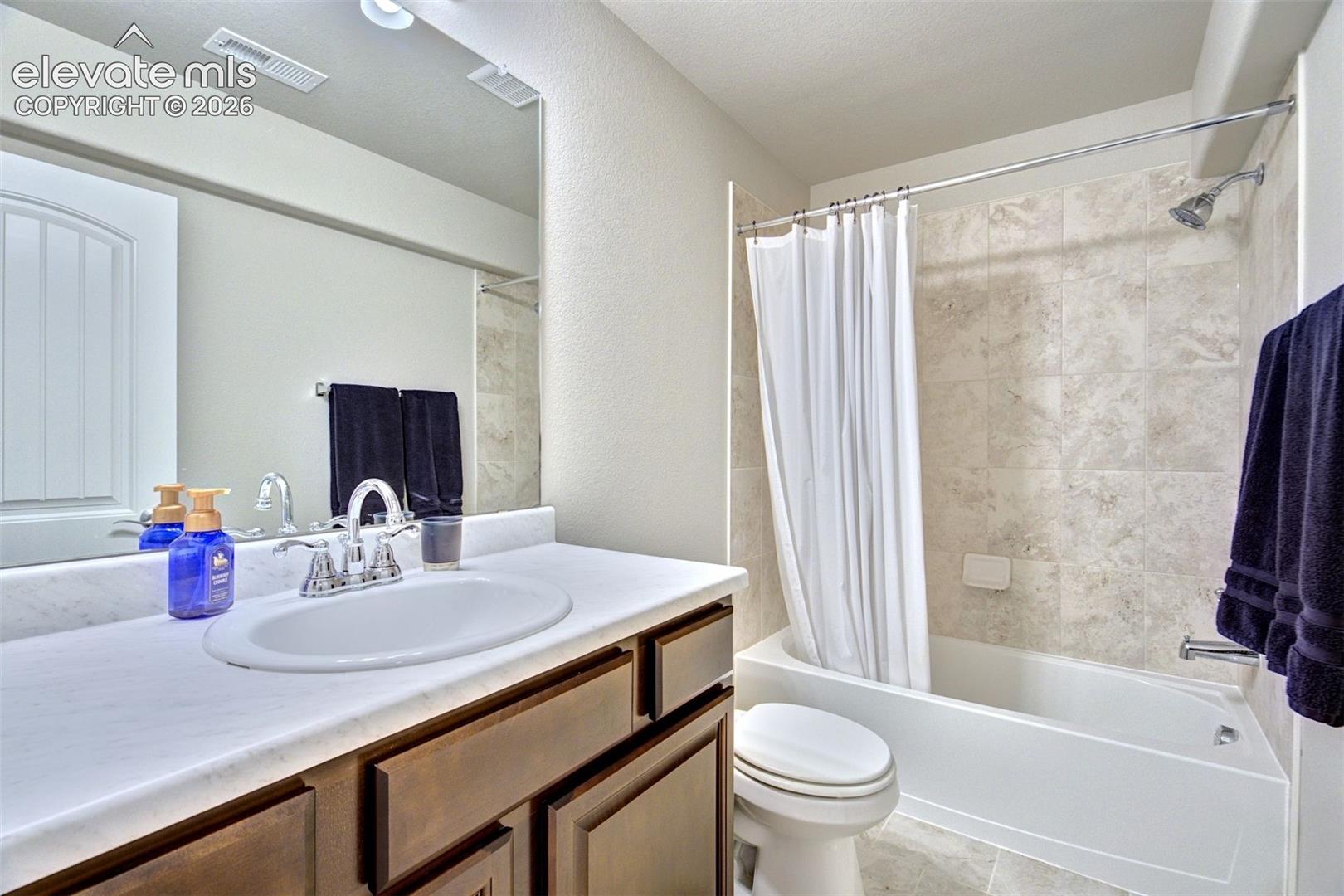 Bathroom featuring a stone-top vanity with an integrated oval basin, polished chrome faucet, full-width mirror, and a tile-surround shower and tub combination