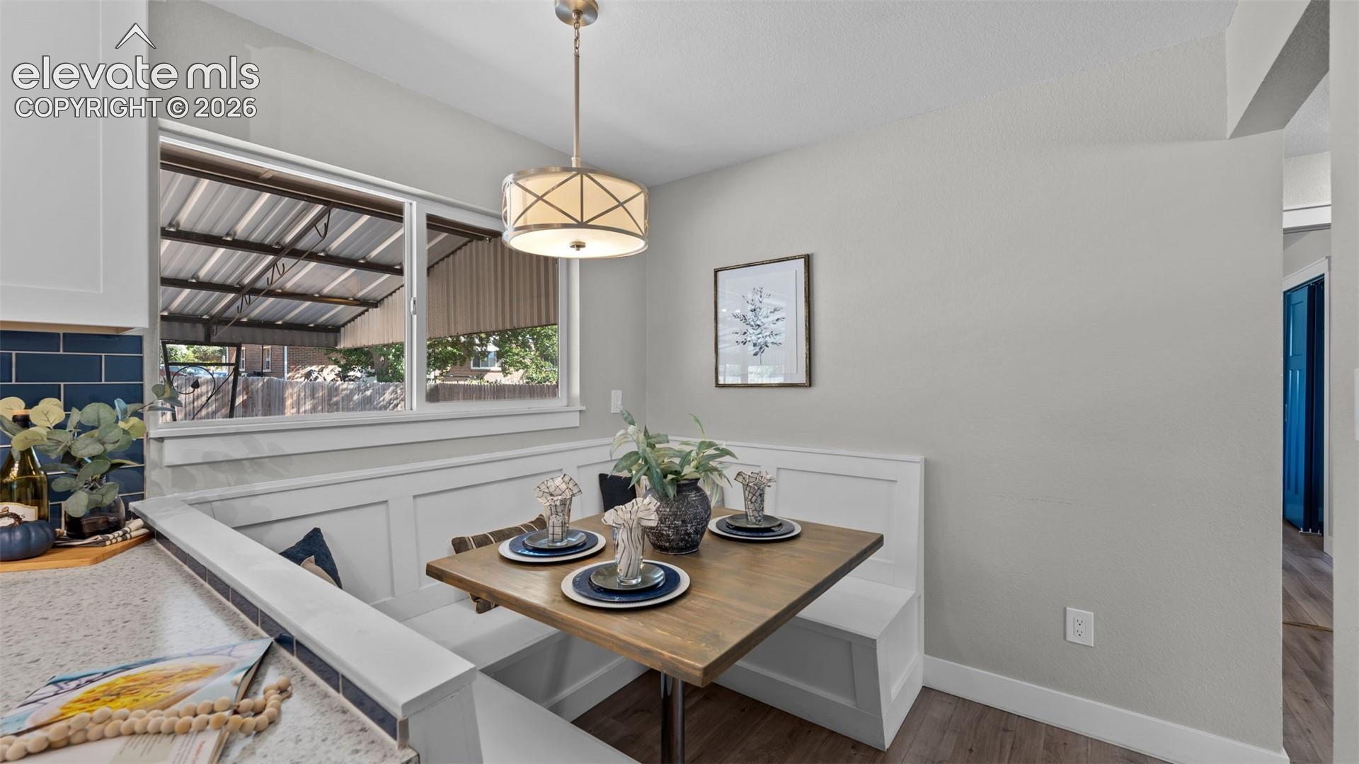 Built-in dining banquette with a wood-finish tabletop, overhead drum pendant light fixture, and wood-finish flooring
