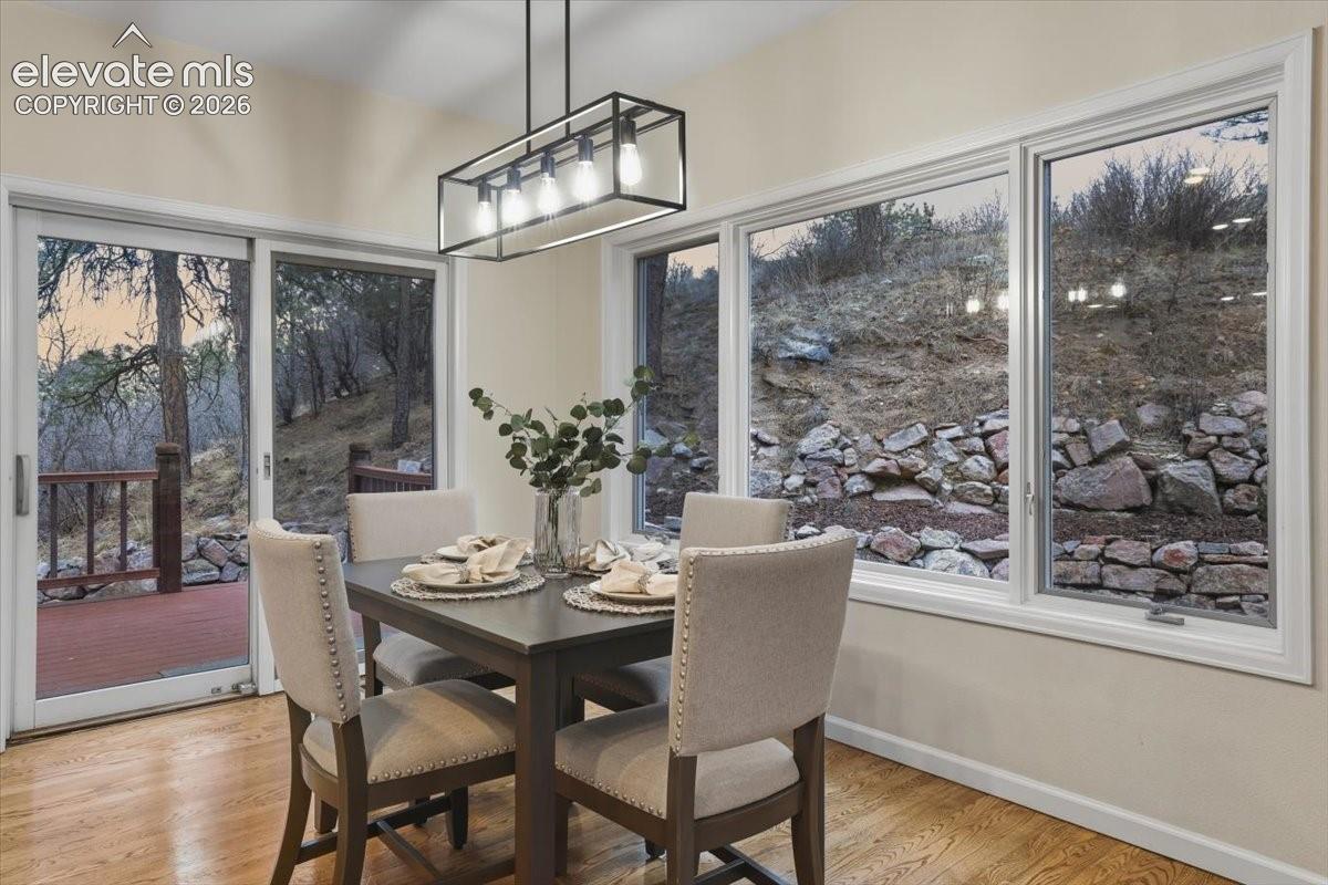 Dining area featuring wood flooring, a contemporary linear chandelier, multiple windows, and a sliding glass door leading to an outdoor deck