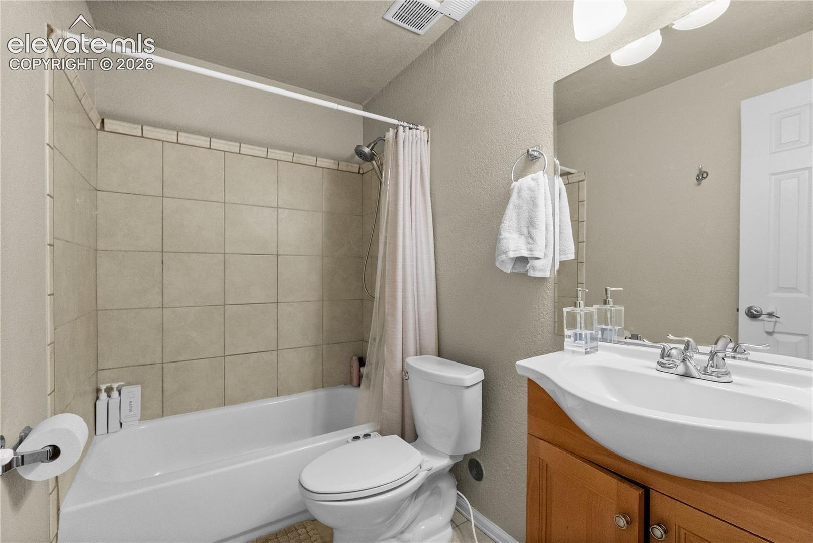 Bathroom featuring a white bathtub, ceramic tile shower surround, toilet, wood-finish vanity with an integrated sink, and an overhead vanity light fixture