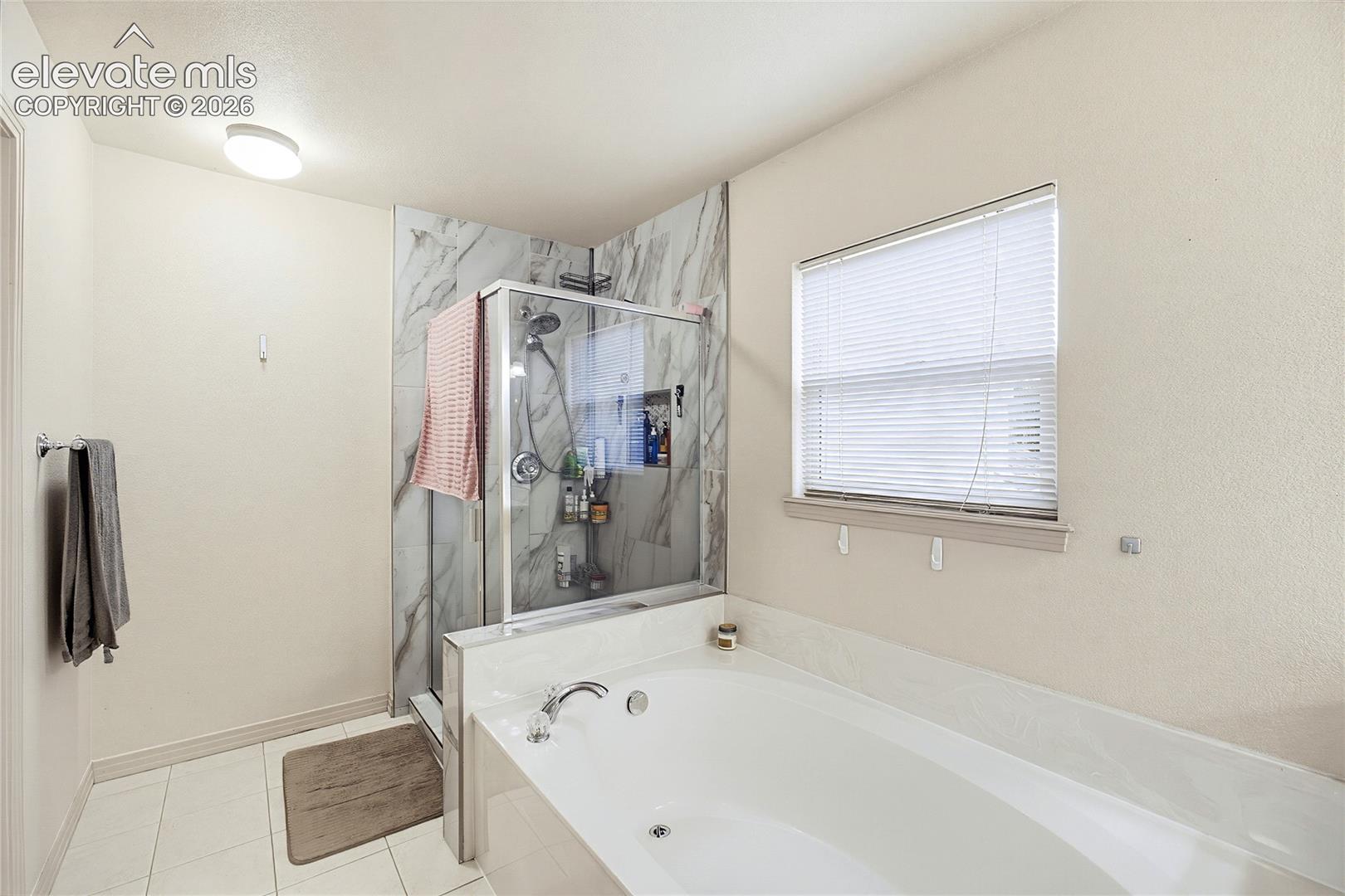 White tile flooring, a built-in soaking tub with deck-mounted faucet, and a separate shower with a glass enclosure and wall-mounted showerhead