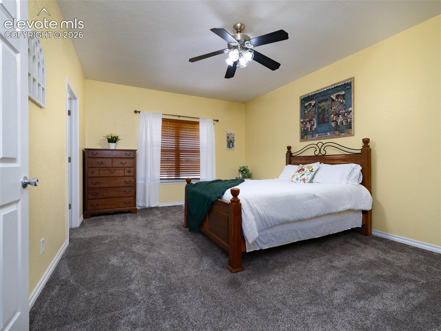 Gray carpeting with white trim, a window with wood blinds, and a ceiling fan with light fixture