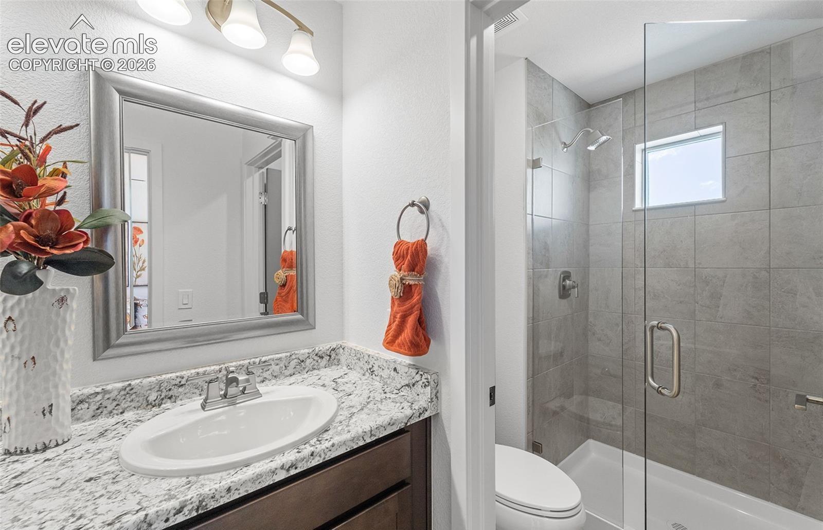 Bathroom featuring a vanity with stone-patterned countertop, under-mount sink, framed mirror, and a walk-in shower with floor-to-ceiling tile surround and glass enclosure
