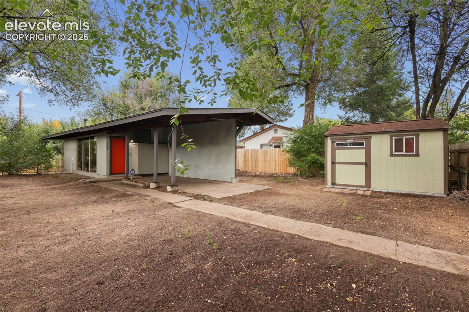 Mid-century modern residence featuring a covered carport, bright red entry door, and a dedicated storage shed