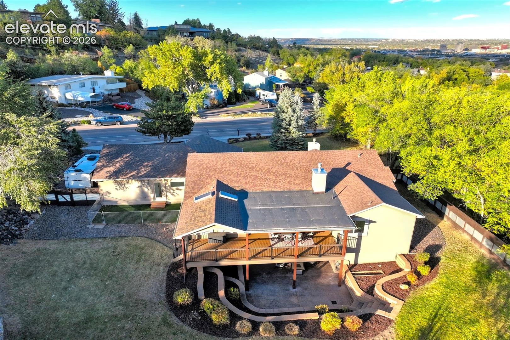 Elevated rear deck with metal railing, two skylights, chimney, concrete patio, and tiered landscaping