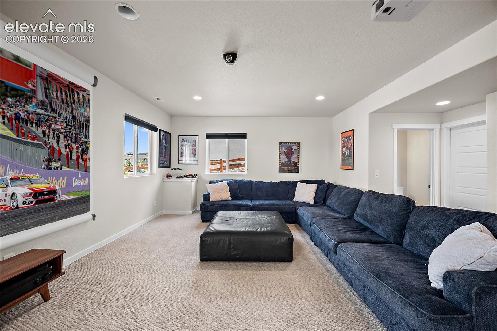 Recessed lighting, large projection screen, wall-mounted projector, multiple windows, and light neutral-toned carpet