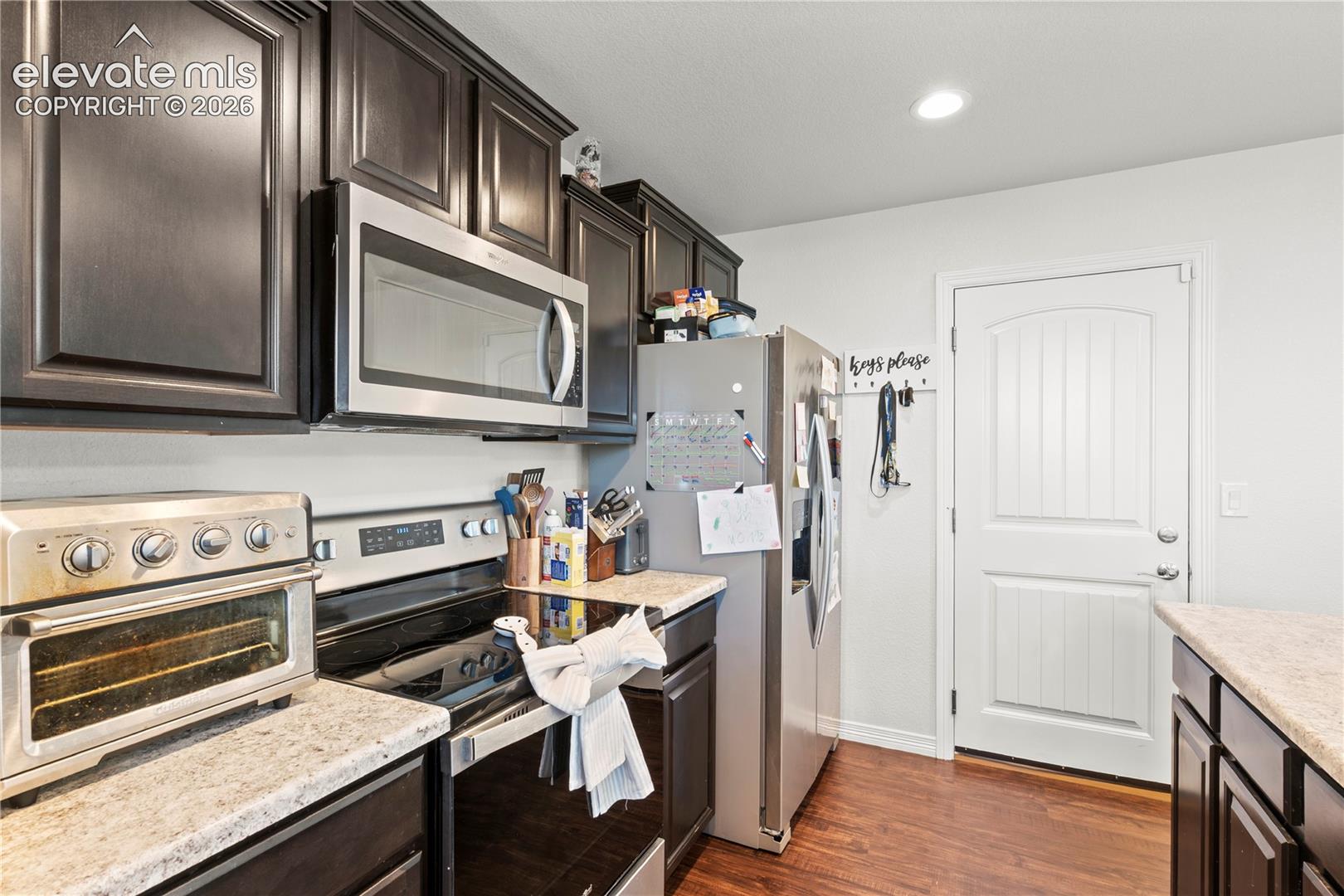 Kitchen featuring dark wood-finish cabinetry, stone-finish countertops, stainless steel appliances, and wood-finish flooring