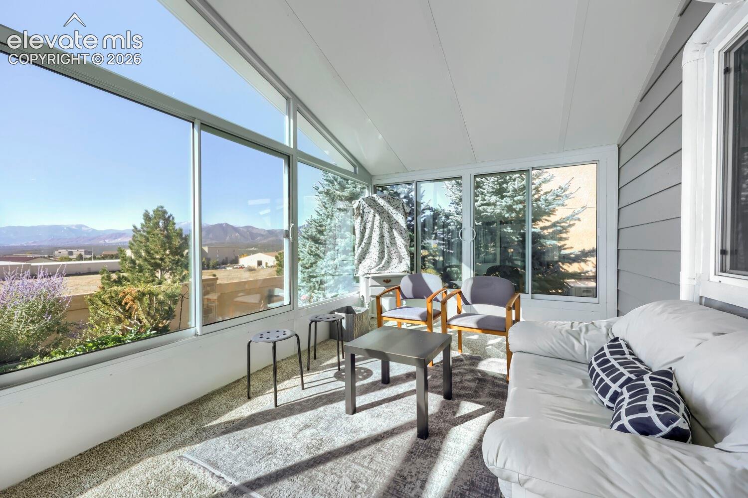Enclosed sunroom featuring expansive floor-to-ceiling windows, vaulted ceiling, and mountainous landscape backdrop
