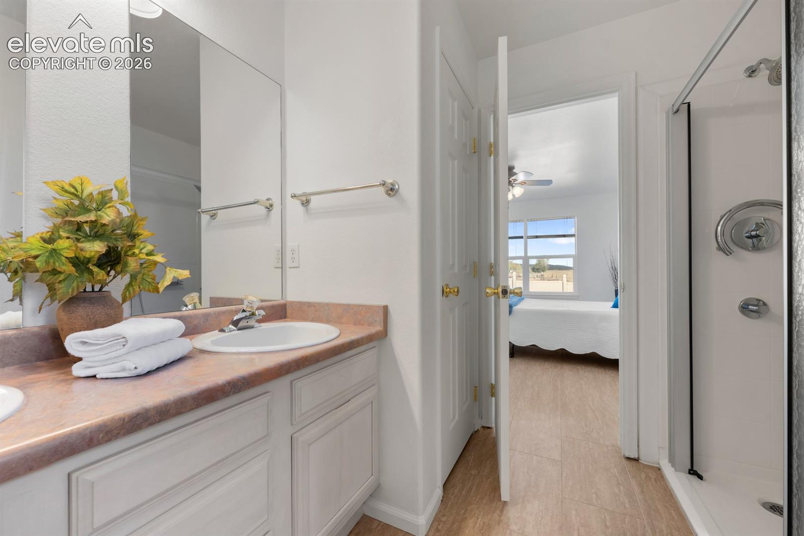Bathroom featuring light-toned cabinetry, solid-surface countertop, dual vanity mirrors, and a walk-in shower with glass enclosure