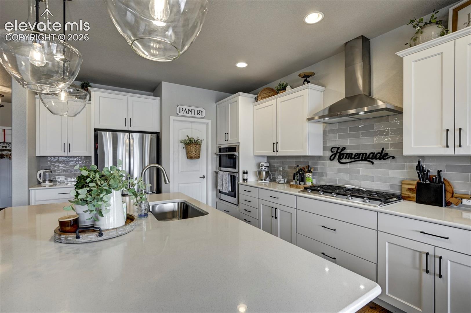 Kitchen featuring white cabinetry, stainless steel appliances, a large island with an undermount sink, a subway tile backsplash, and overhead pendant lighting