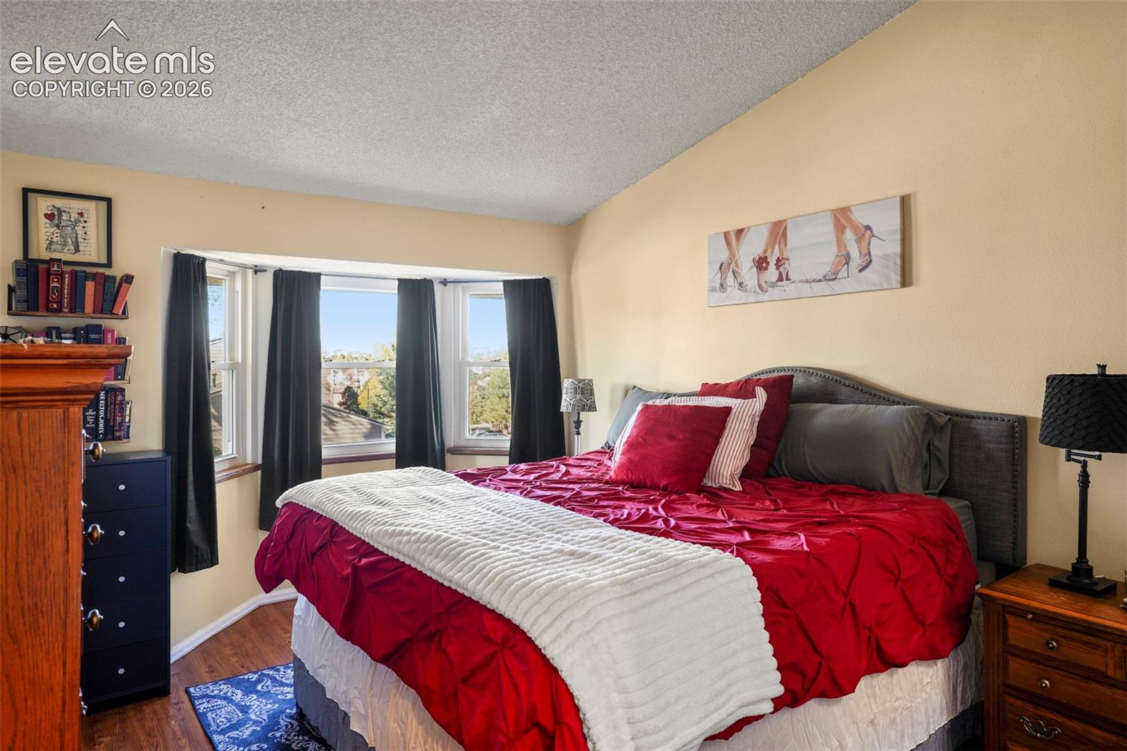 Room featuring a vaulted ceiling, bay window, and wood-finish flooring