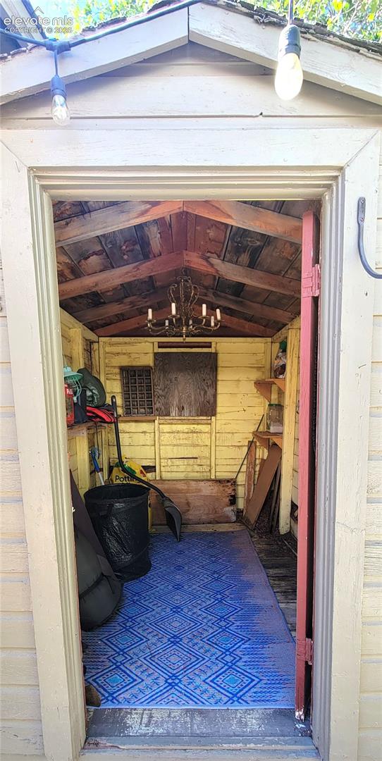 She Shed, located off of back patio. Gable roofline with exposed wood beams, interior wood-paneled walls, and a mounted chandelier fixture