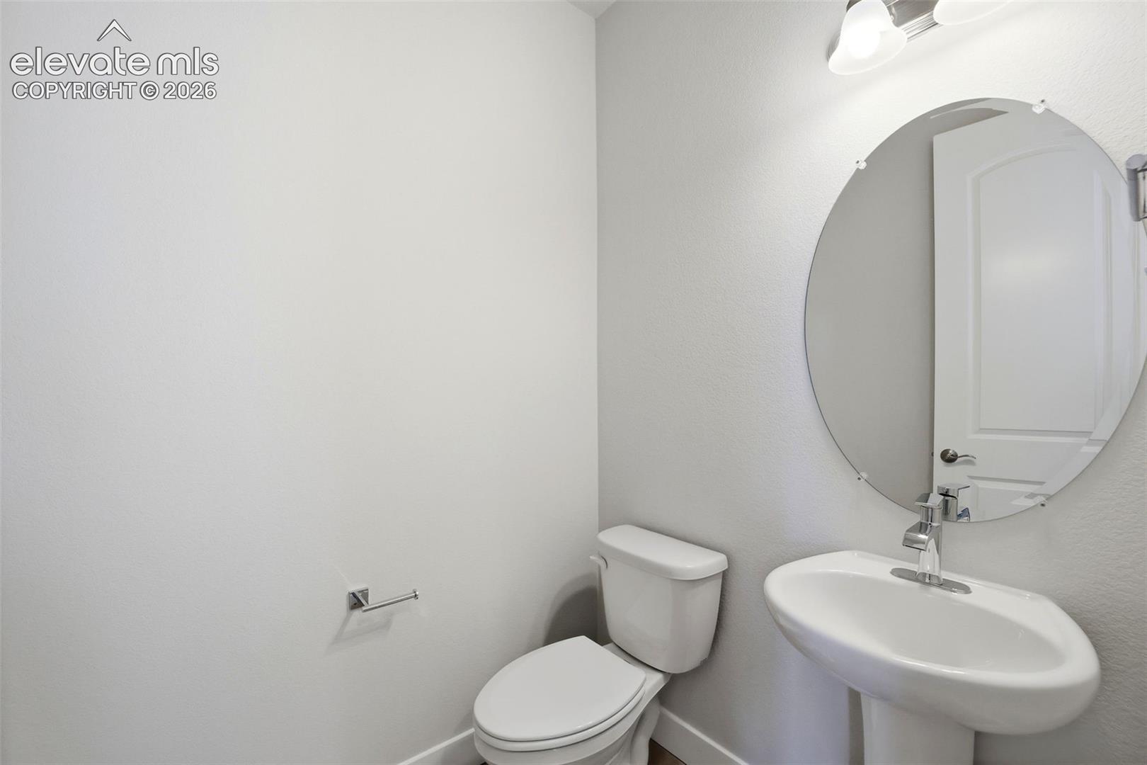 Pedestal sink with chrome faucet, circular frameless mirror, and dual-light vanity fixture