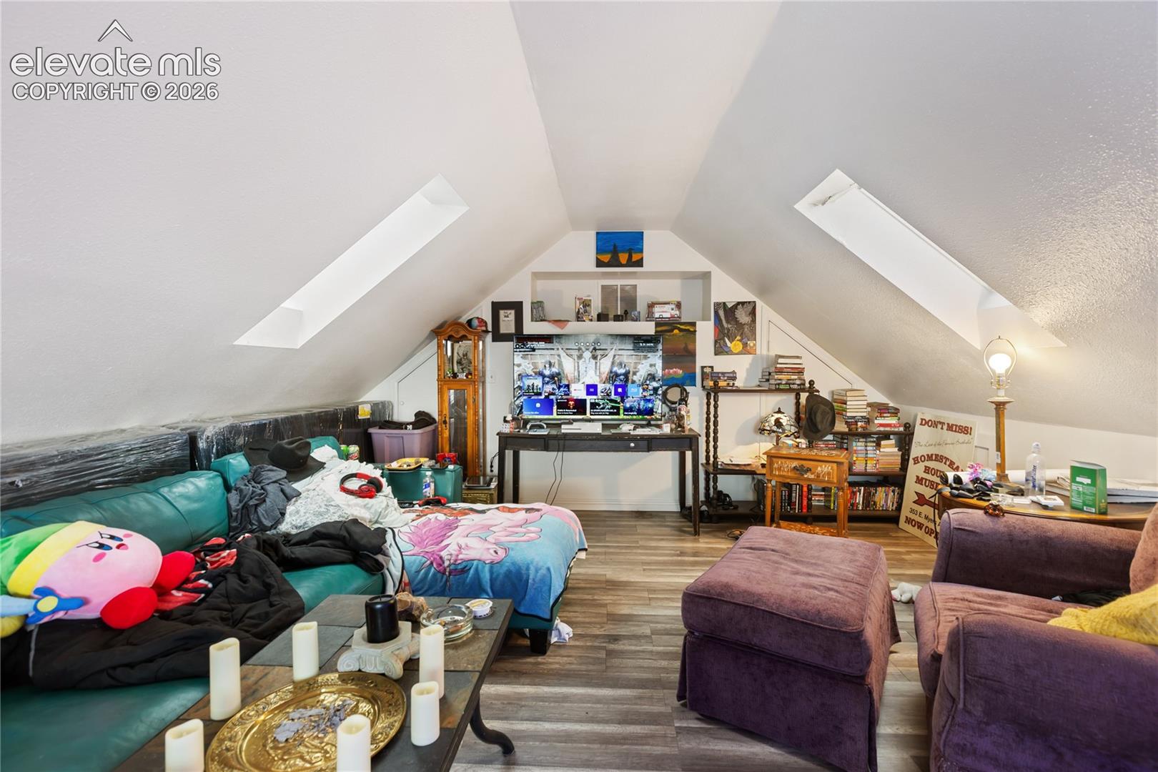 Finished attic space featuring dual skylights, wood-finish flooring, and a recessed wall niche