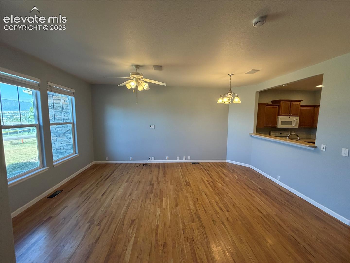 Hardwood flooring throughout, two large windows, ceiling fan, and a pass-through opening to the kitchen