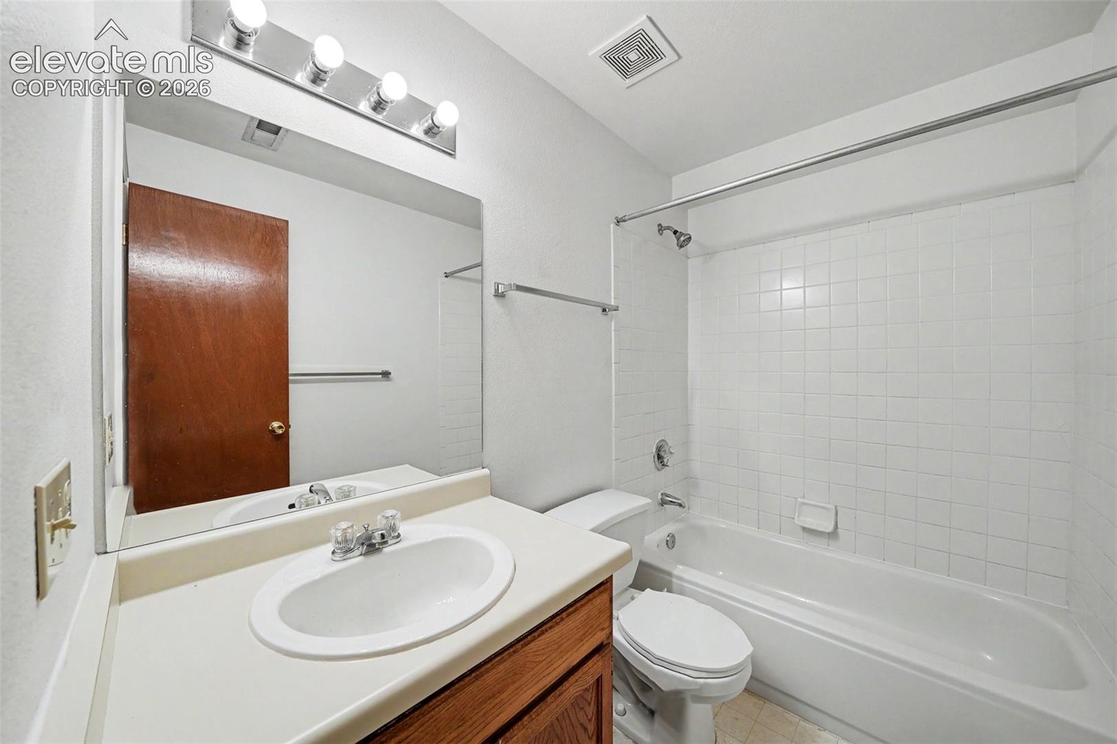 Bathroom featuring a wooden vanity, integrated basin, wall-mounted mirror, four-light fixture, and a tub-shower combination with white tile surround