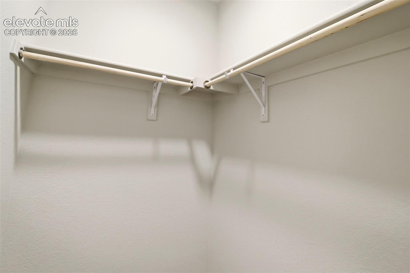 Storage space featuring wraparound shelving and integrated hanging rods with white wall-mounted hardware
