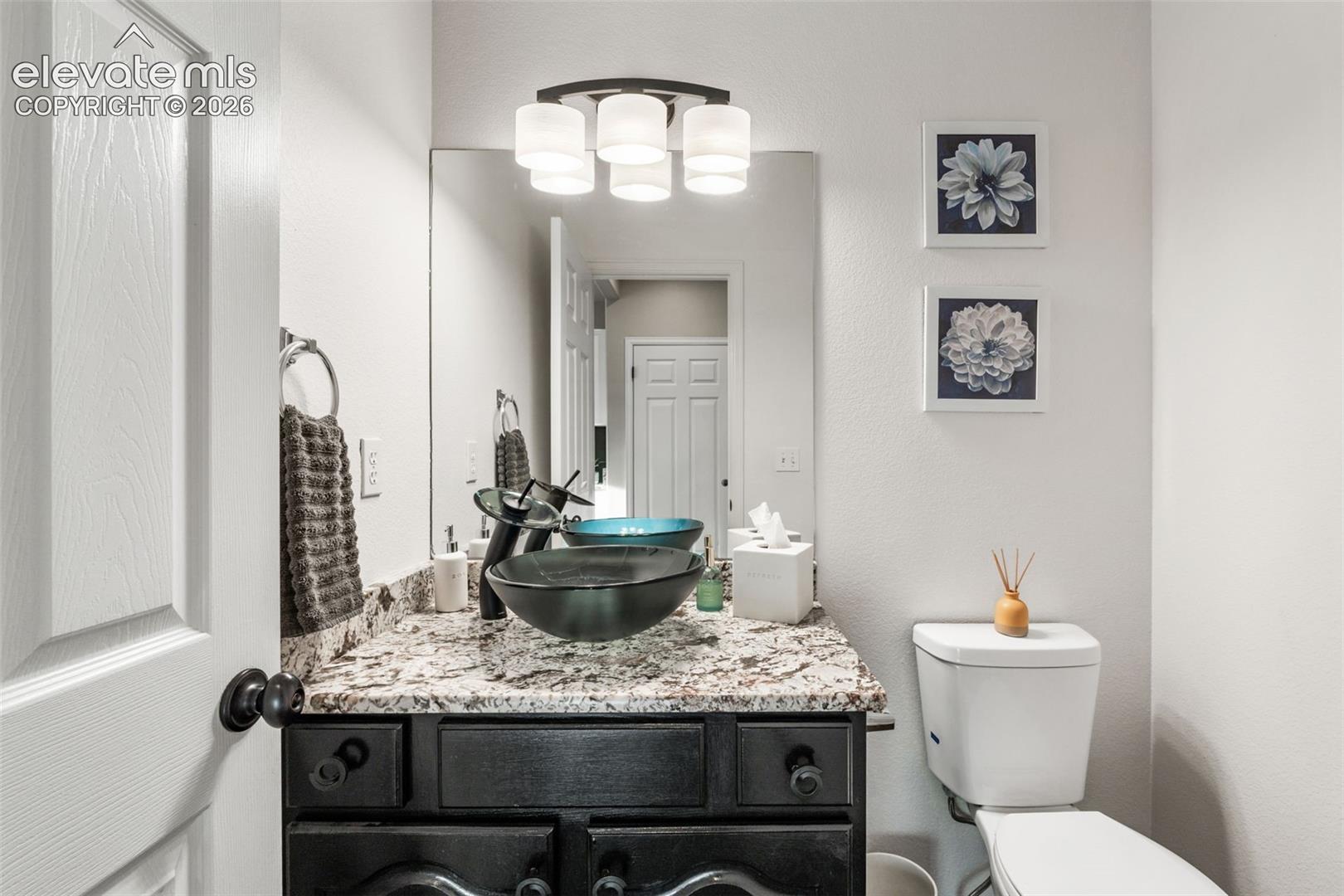 Vanity featuring a dark-toned base cabinet, stone countertop, and dark-finished vessel sink with a coordinating faucet