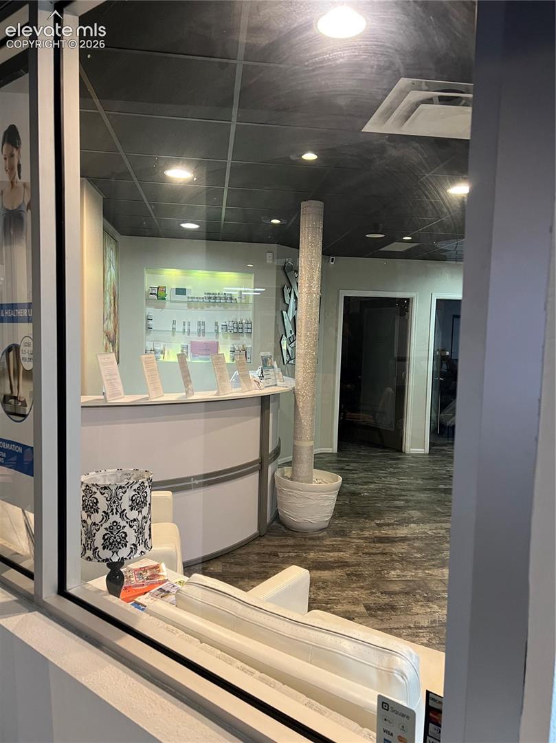 Reception area featuring a curved service desk, wood-finish flooring, recessed lighting, drop ceiling, and a decorative pillar
