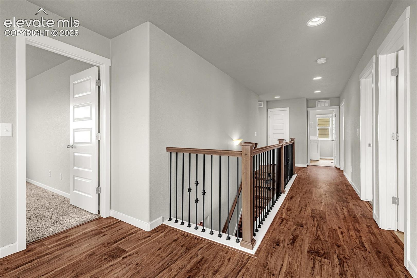 Wood-finish flooring, staircase with wood handrail and wrought iron balusters, recessed lighting, and white paneled doors
