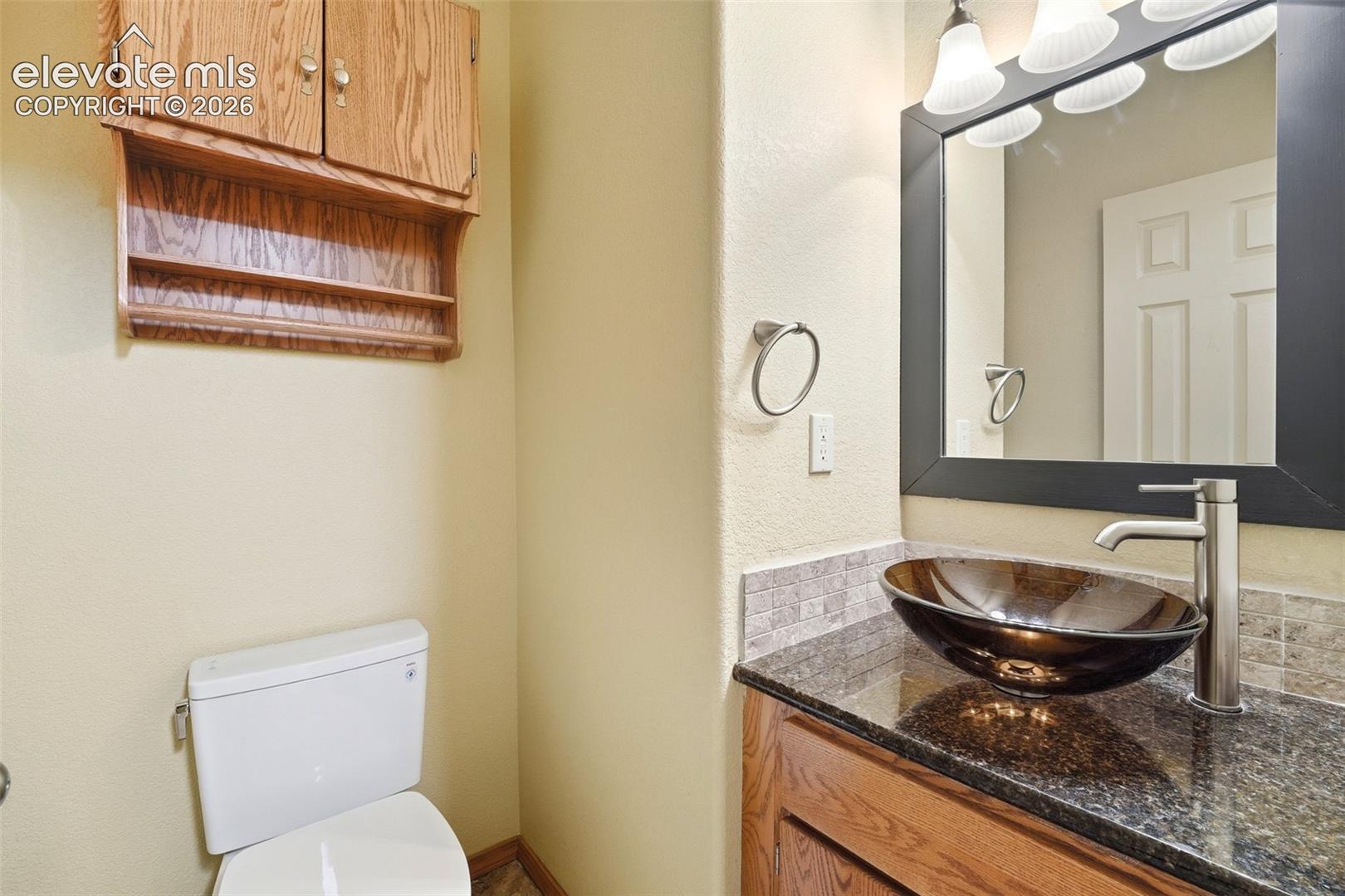 Bathroom vanity featuring a vessel sink, dark countertop, and wood-finish cabinetry