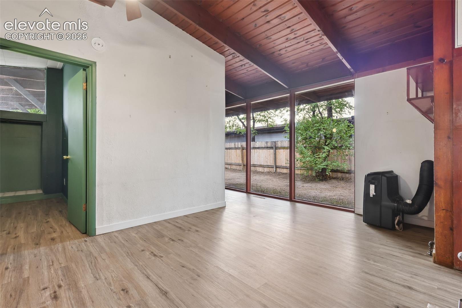 Wood-finish flooring, exposed beam ceiling, full-height windows, and a green painted door