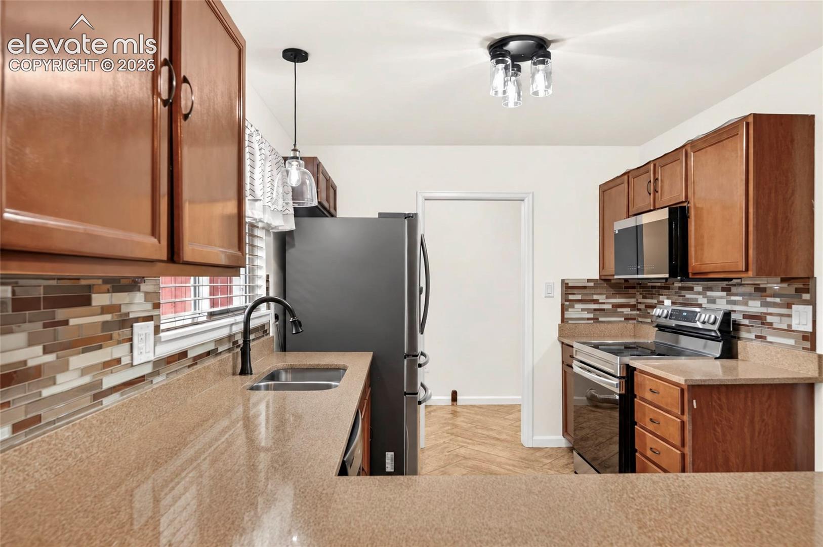 Kitchen featuring wood cabinetry, solid-surface countertops, multicolored stone tile backsplash, stainless steel appliances, and multi-light fixtures