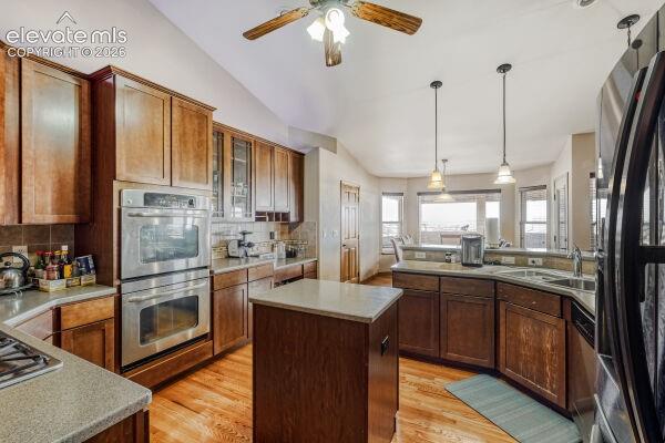 Kitchen featuring wood-finish cabinetry, stainless steel double wall ovens, a center island with a light-toned countertop, wood-finish flooring, and a curved peninsula with a double basin sink and pendant lighting