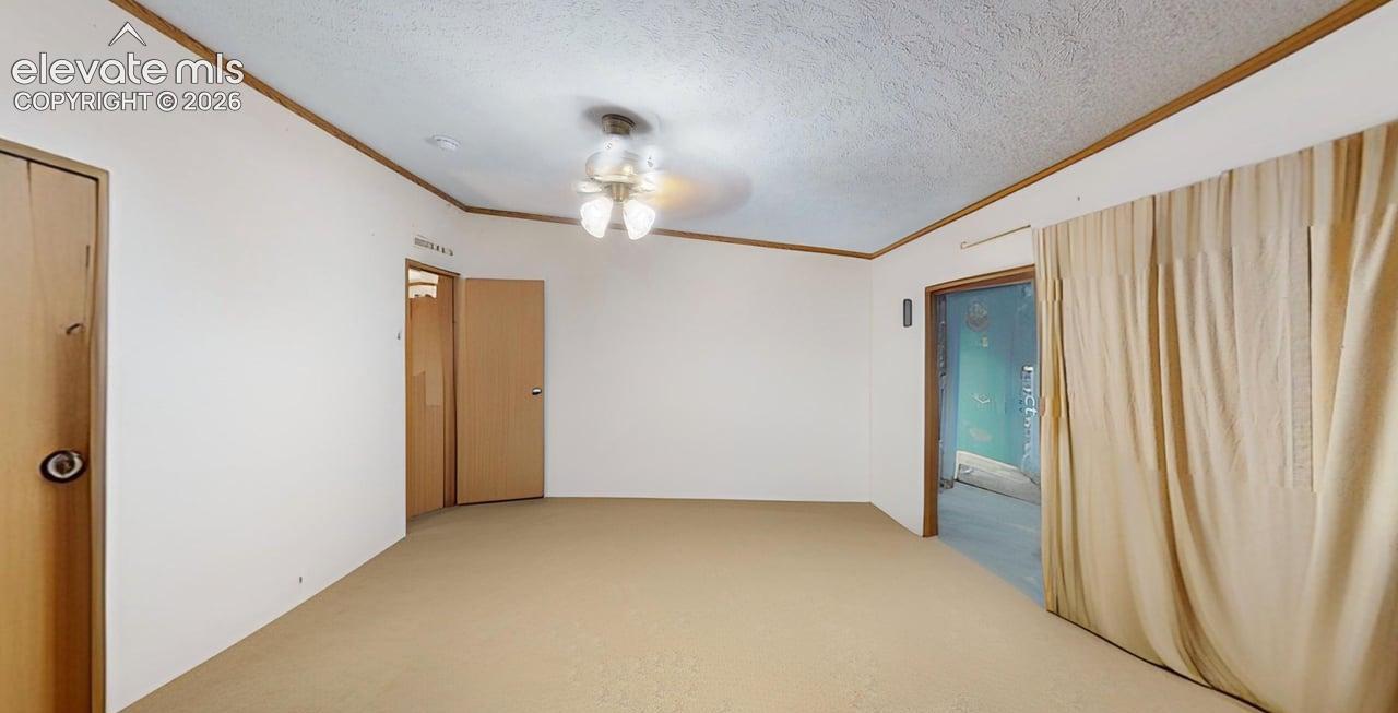 Empty room with a textured ceiling, crown molding, light carpet, and a ceiling fan