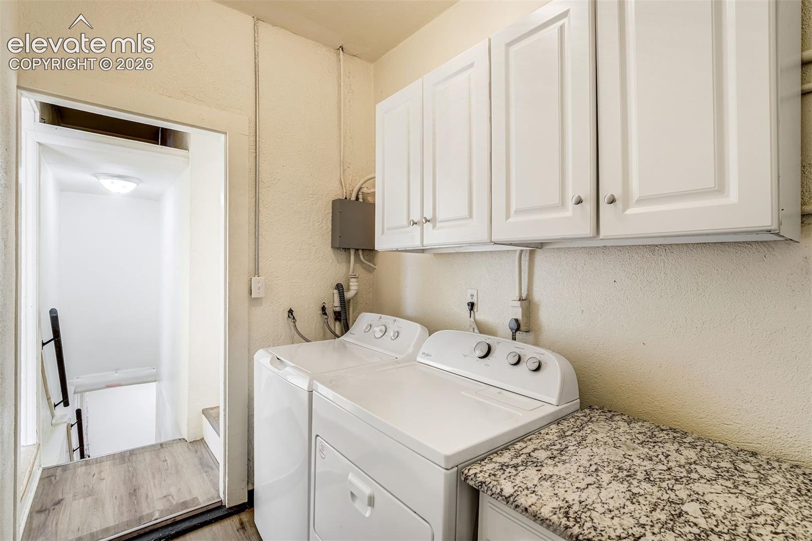 Laundry area featuring white shaker-style wall cabinets, speckled stone-finish countertop, and dedicated utility hookups