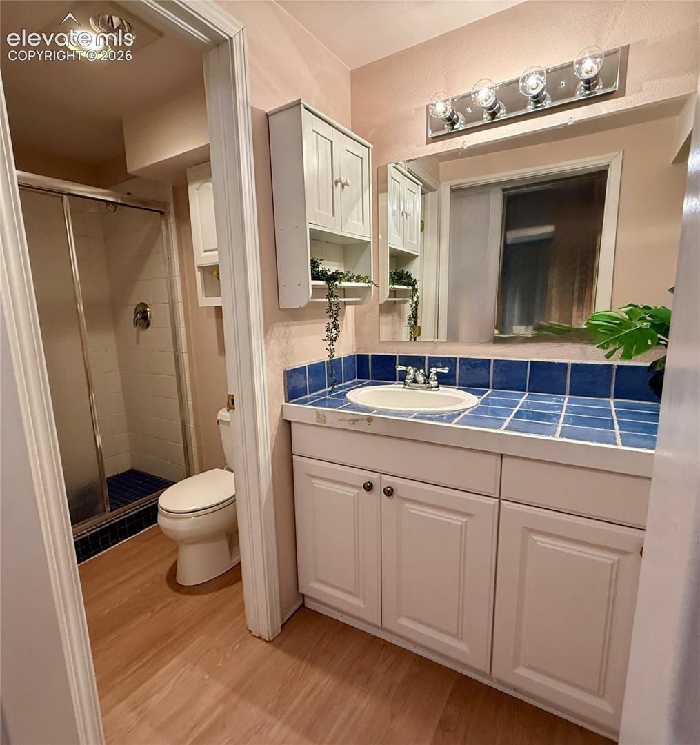 Bathroom featuring a vanity with white cabinetry, a tile countertop, a sink, a wall-mounted storage cabinet, and a shower with a sliding glass door