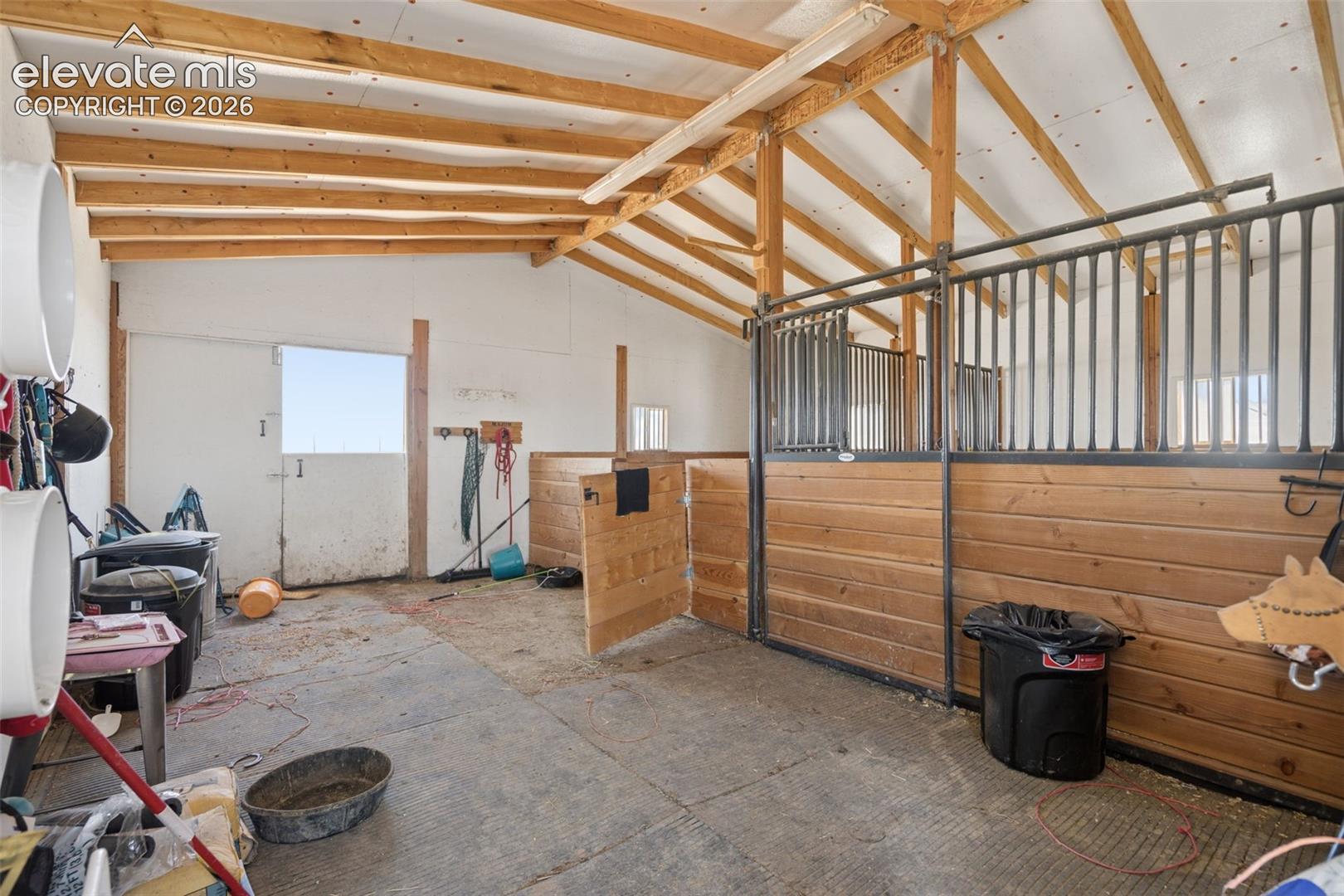 Stable facility featuring vaulted exposed-rafter ceilings, wood-plank stall partitioning, black metal stall grilles, and Dutch door entry