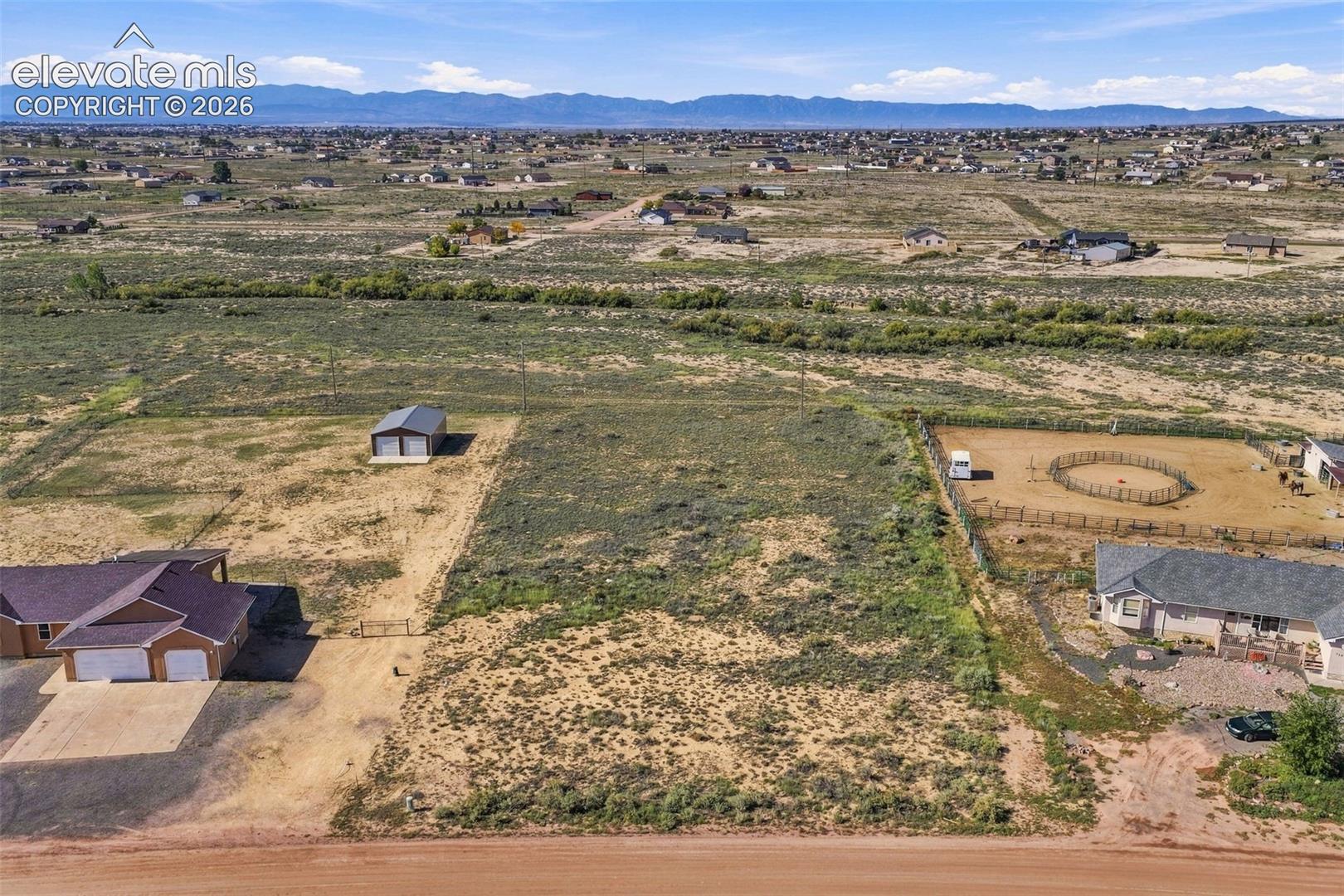 Expansive land parcel featuring a detached metal-roofed structure, mountain backdrop, and vast desert landscape