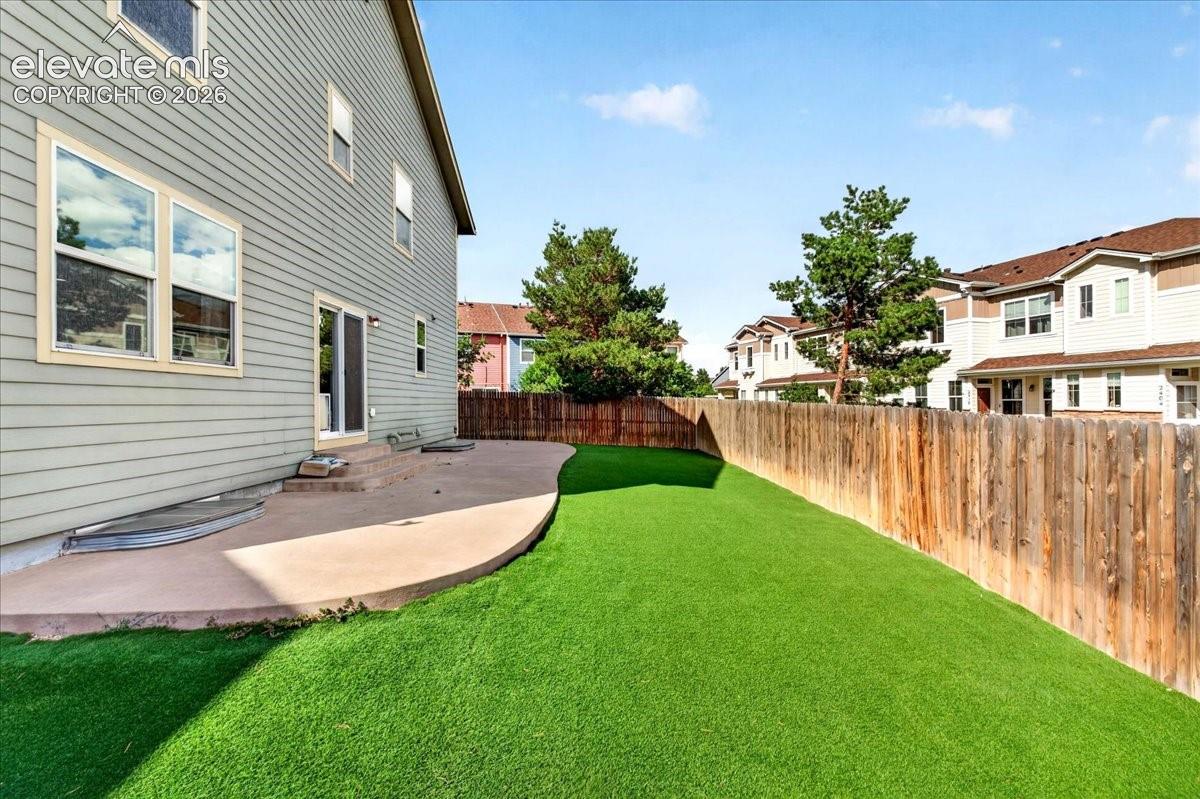 Rear exterior with siding, sliding glass door, curved concrete patio, artificial turf, and wood privacy fence
