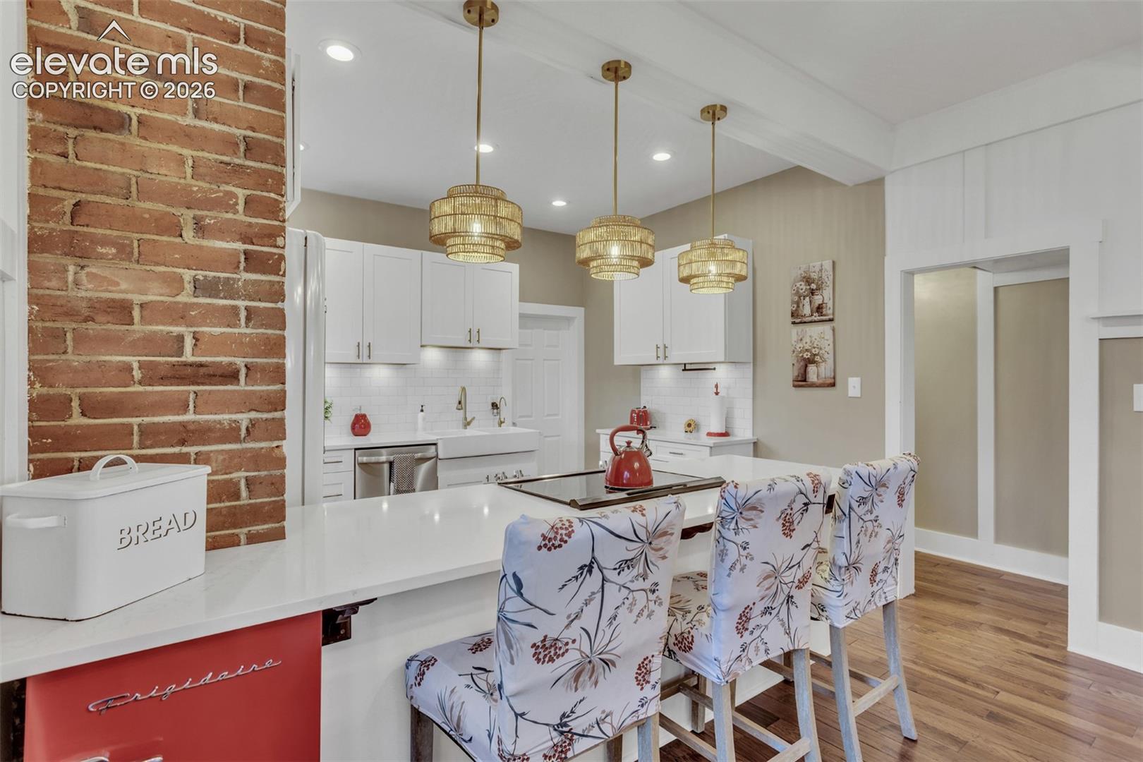 Open-concept kitchen featuring an exposed brick pillar, white shaker cabinetry, and a white subway tile backsplash