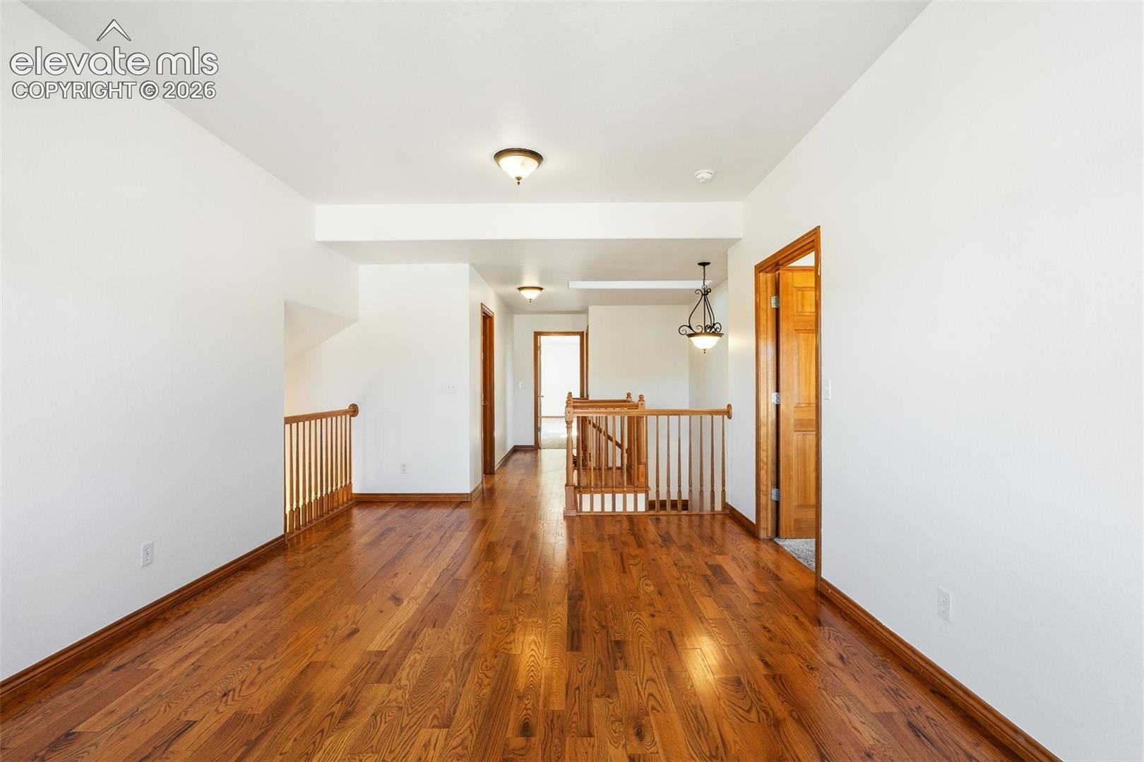 Open interior space featuring wood-finish flooring, wood-toned railings, and multi-light pendant and flush-mount fixtures