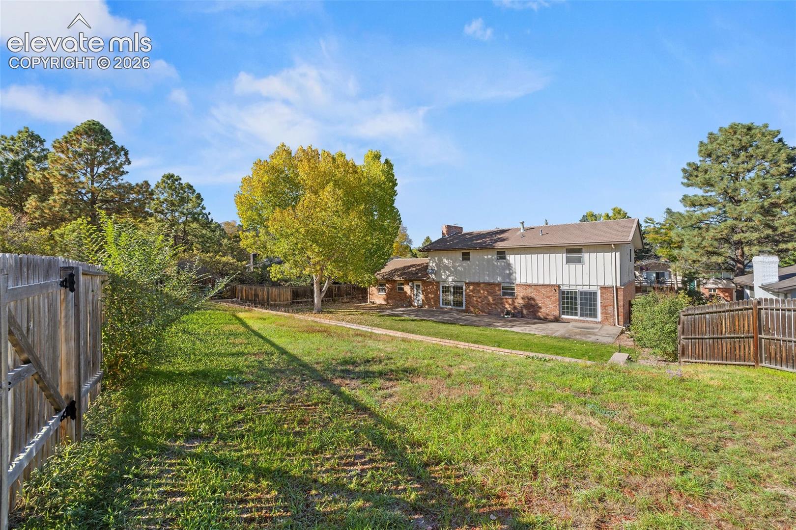 Expansive backyard featuring a concrete patio, wood privacy fencing, and mature trees