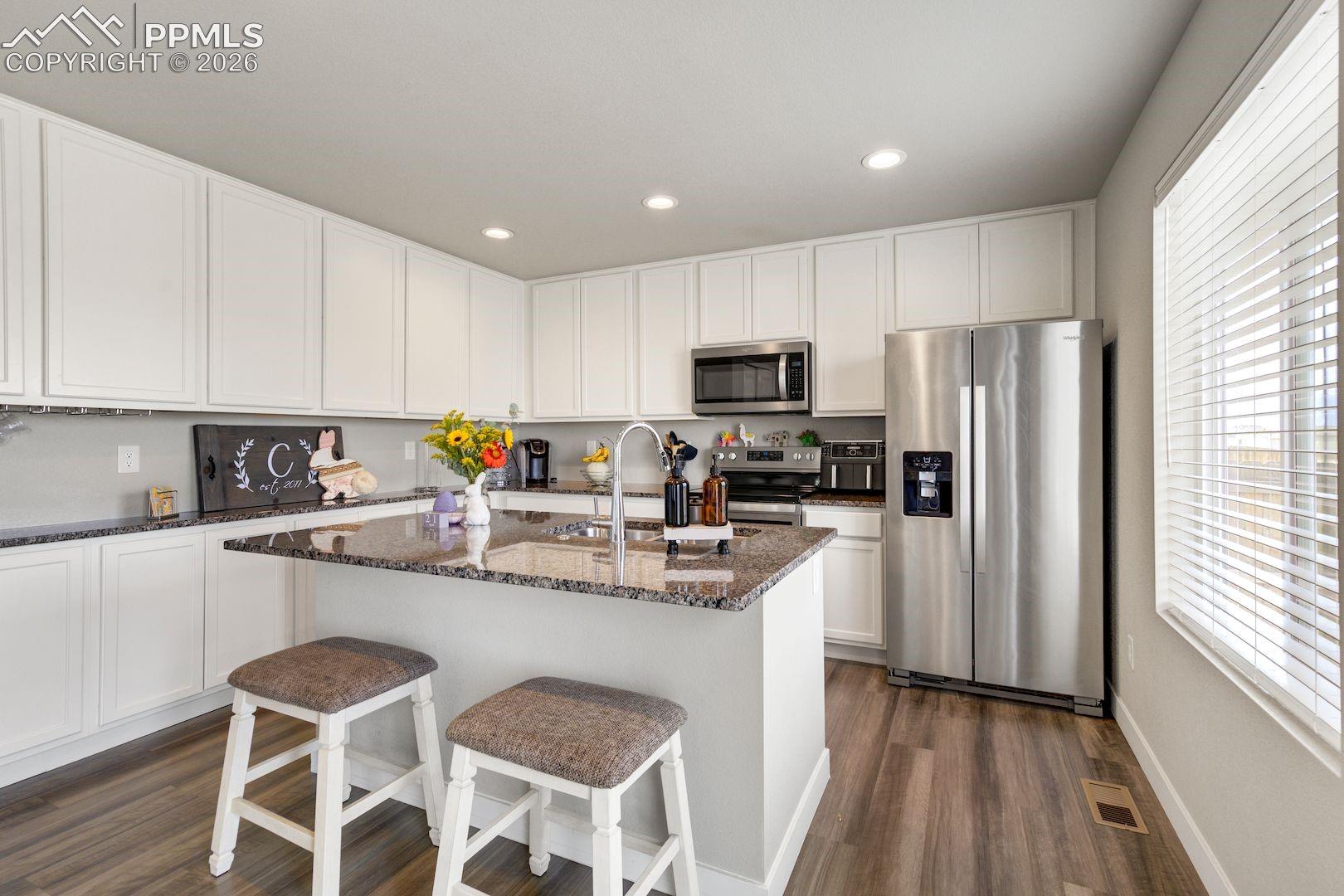 Kitchen featuring appliances with stainless steel finishes, dark stone counters, white cabinetry, a center island with sink, and a breakfast bar